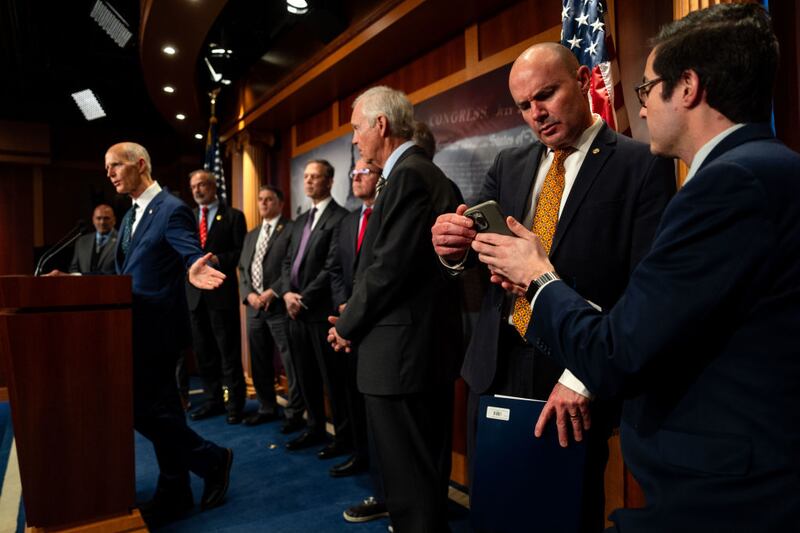 An aide shows a cell phone to Republican Sen. Mike Lee during a news conference on the proposed continuing resolution to extend government funding through next year.