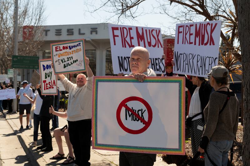 People protest against Tesla and Elon Musk outside of a dealership in Palo Alto, California, on Saturday.
