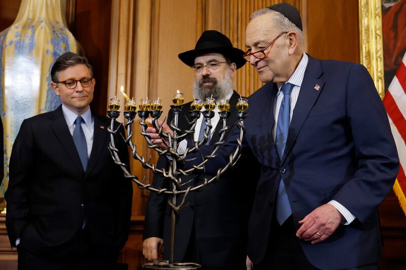Mike Johnson and Rabbi Levi Shemtov look on as Chuck Schumer lights a Menorah during a Hanukkah reception at the U.S. Capitol Building on December 17, 2024 in Washington, D.C.