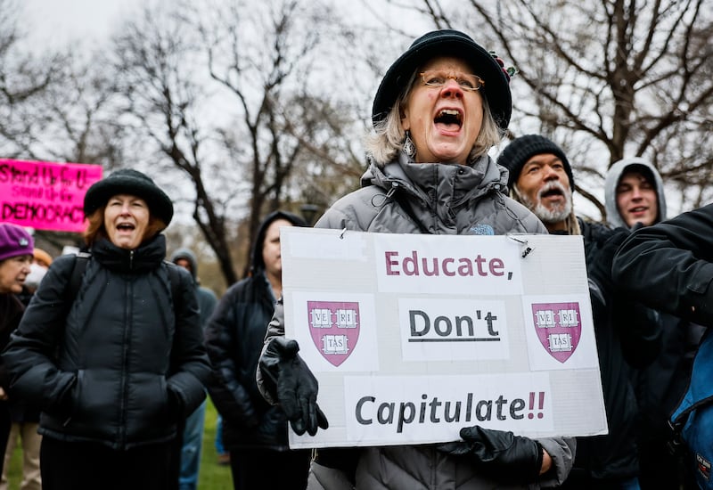A protester holds a sign reading "Educate, Don't Capitulate!!" and Harvard University's shields during a rally at Cambridge Common urging the Ivy League institution to resist President Trump's influence.