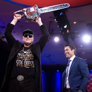 Elon Musk wields a chainsaw as he leaves the stage with Newsmax anchor Rob Schmitt at the Conservative Political Action Conference (CPAC).