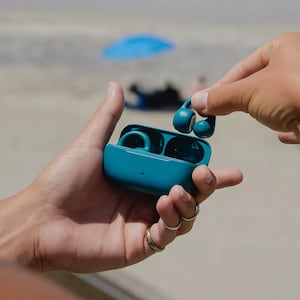 A person holding a pair of teal JLab wireless earbuds open in their hand.