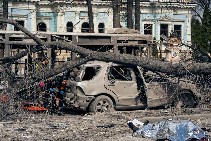 A blown out bus and car and a body covered in a silver blanket after Russia's Palm Sunday attack in the Ukrainian city of Sumy.