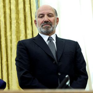 Donald Trump sits at his desk in the Oval Office while Howard Lutnick looks over his shoulder.