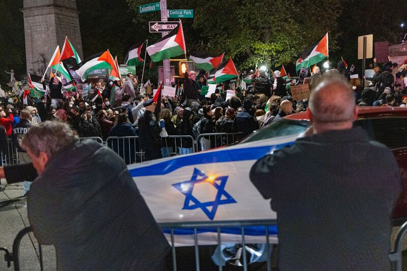A picture of counter protestors holding an Israeli flag across the street where pro-Palestinian protesters gather for a march.