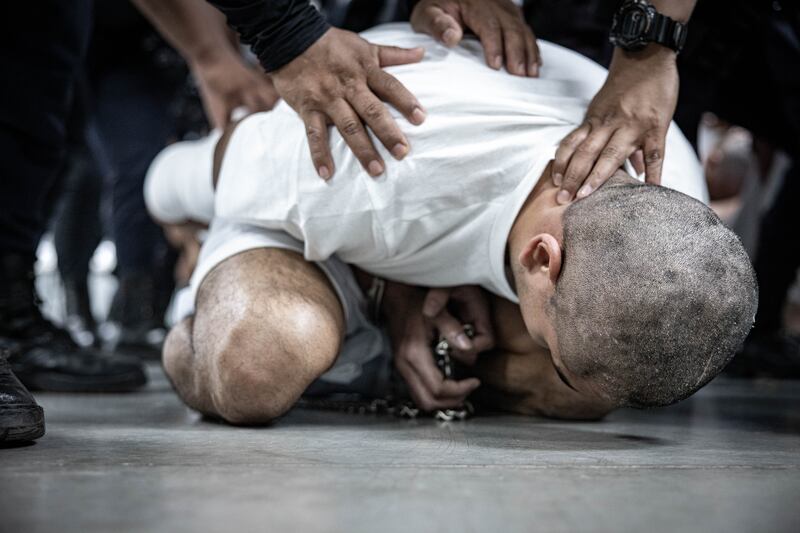 An inmate is restrained by a guard at CECOT.