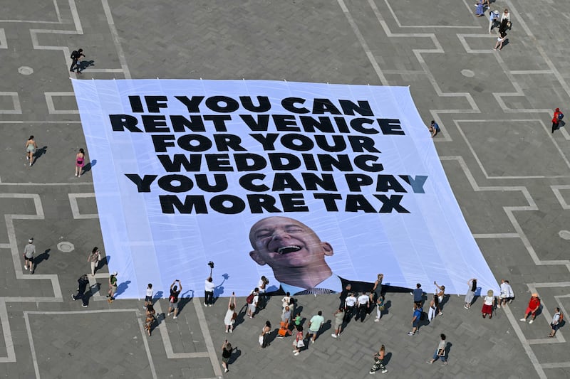 Activists of international environmental group Greenpeace deploy a giant banner displaying a picture of Jeff Bezos and reading "If you can rent Venice for your wedding you can pay more tax" at St Mark square  in Venice on June 23, 2025. Venice will host the wedding of Amazon Founder and CEO Jeff Bezos and journalist Lauren Sanchez before the end of the month with more than 200 guests expected to attend. (Photo by Stefano Rellandini / AFP) (Photo by STEFANO RELLANDINI/AFP via Getty Images)