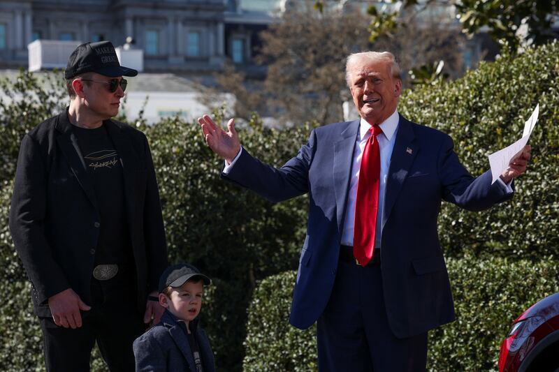 Donald Trump talks to the media while Elon Musk and his four-year-old son stands nearby.
