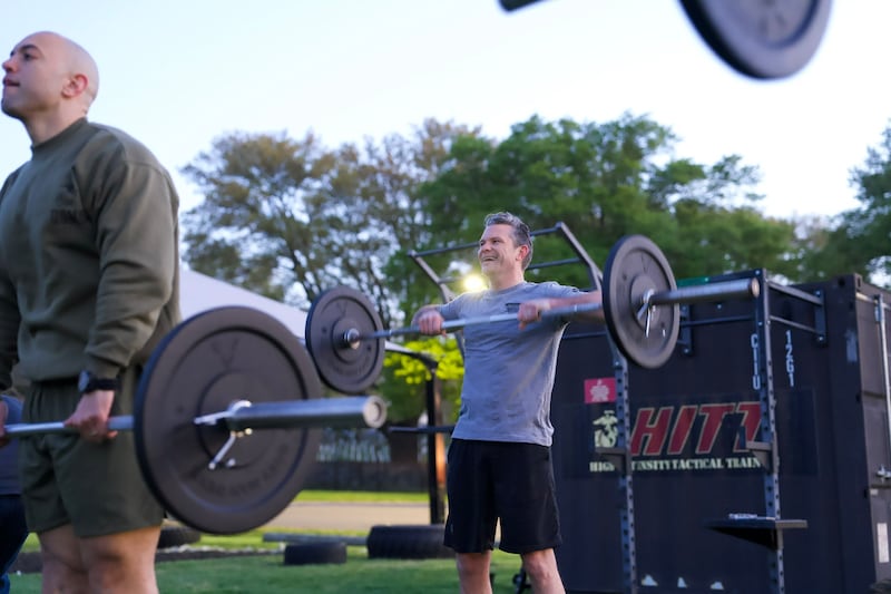 Pete Hegseth lifts weights outside in a t-shirt and shorts.